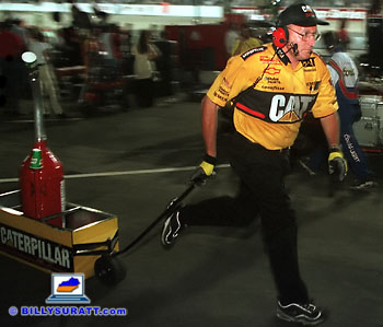 A Caterpillar team member rushes down pit row with a can of gas. Panning the camera combined with a slow shutter speed and rear curtain flash sync helps convey movement and a sense of urgency. (Copyright 1998 Billy Suratt)
